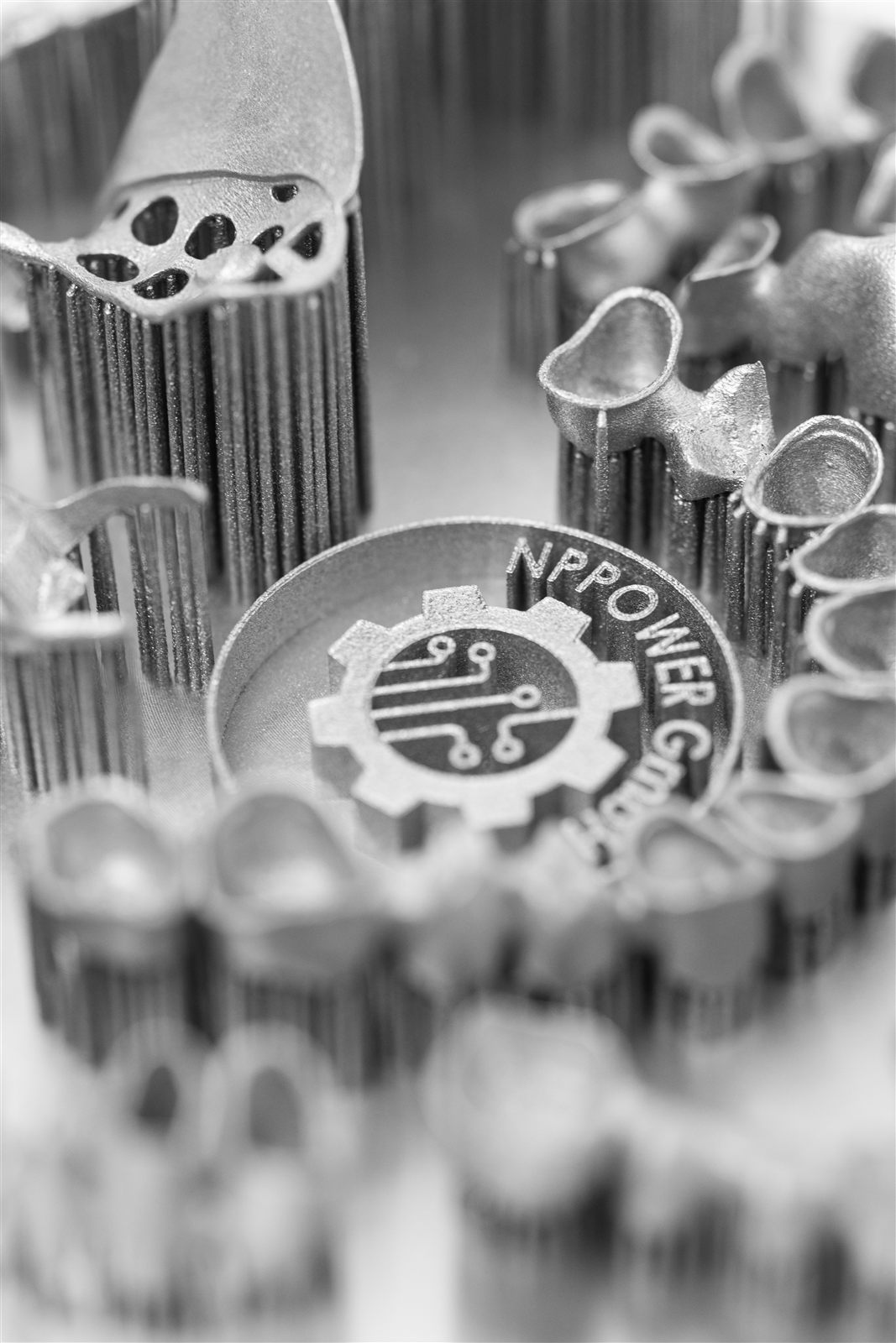 Metal dental crowns printed on thin support pins next to an NPPower logo coin